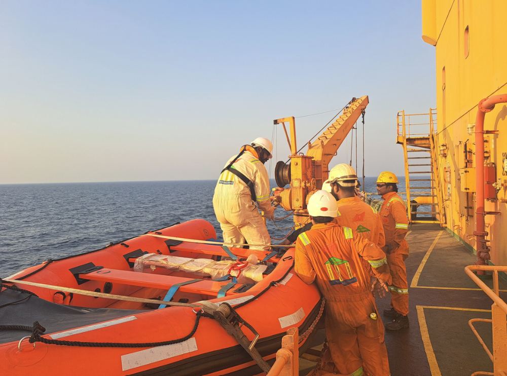 Crew in coveralls and hard hats handling equipment on an offshore vessel deck
